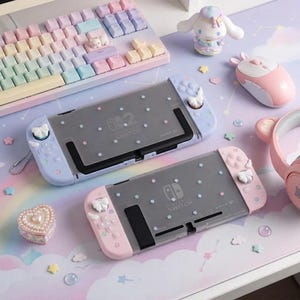 May include: Two Nintendo Switch consoles with custom pastel-colored protective cases featuring small star decals. One console has light blue controllers with white bow accents, while the other has light pink controllers with white bow accents.