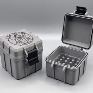 May include: Two square, light grey storage cases with black latches. One case is closed, featuring a circular graphic of a scientist with the text "Yeah, Science!" on the lid. The other case is open, revealing a grid-like interior compartment.