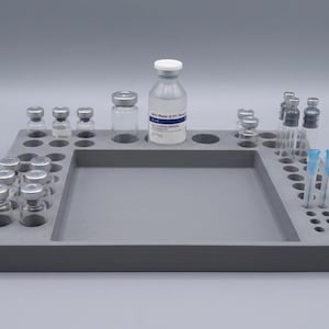 May include: A grey rectangular organiser tray with multiple circular cutouts for vials and syringes. The tray holds several clear glass vials with silver caps, one larger vial labelled Bacteriostatic Water, and a clear plastic syringe with a blue needle.