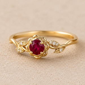Peut inclure: Une bague en or avec une pierre centrale rubis rouge profond de forme ronde, sertie dans une monture florale. L'anneau présente un travail de métal délicat en forme de vigne avec de petites pierres claires incrustées en forme de feuilles.