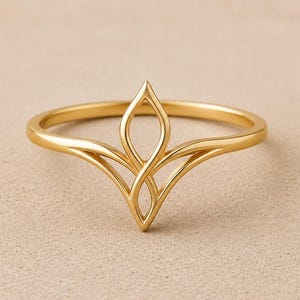 May include: A gold ring featuring a central V-shaped design composed of two interlocking, pointed oval loops that extend upwards from the band. The metal has a smooth, polished finish, and the structure creates a symmetrical, openwork focal point.