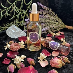 May include: A clear glass dropper bottle and a smaller glass roller bottle, both labeled House of the Crescent Vow with a crescent moon icon. The bottles contain liquid with visible dried flower petals and are surrounded by loose dried rose petals and buds.