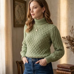 Könnte beinhalten: Ein salbeigrüner Rollkragenpullover mit einem strukturierten Zopfstrickmuster mit Rautenmotiv, langen Ärmeln mit gerippten Bündchen und einem hohen gerippten Kragen. Der Pullover wird mit einer dunkelblauen Jeans mit sichtbaren Vordertaschen kombiniert.