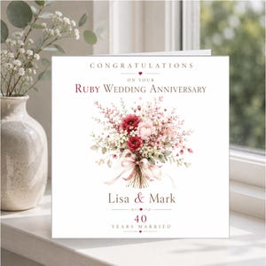 May include: A square greeting card with white background featuring a floral bouquet illustration in shades of red, pink, and white. Text reads: CONGRATULATIONS ON YOUR RUBY WEDDING ANNIVERSARY, Lisa & Mark, 40 YEARS MARRIED. The design includes small red heart accents.