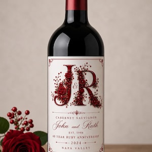 Può includere: Una bottiglia di vino in vetro scuro con un'etichetta personalizzata che presenta grandi lettere floreali rosse JR, i nomi John e Ruth, il testo EST. 1984, 40 YEAR RUBY ANNIVERSARY, 2024 e NAPA VALLEY su sfondo crema con bordi decorativi rossi.