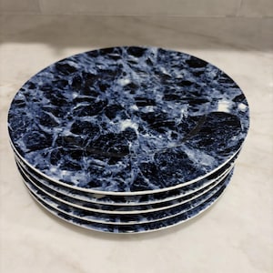 May include: A stack of five round plates featuring a dark blue and white marbled pattern. Each plate has a smooth, glossy finish with a distinct veined design that mimics natural stone, creating a cohesive look across the entire set of dinnerware.