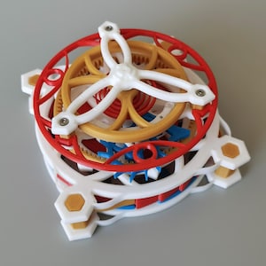 May include: A mechanical model featuring a white, red, gold, and blue gear assembly. The structure includes a white frame with hexagonal corners, a central gold wheel, and a red circular outer ring, all held together by small metal screws.
