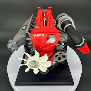 Pode incluir: Um modelo detalhado de motor Nissan Skyline GT-R RB26 com uma tampa de válvulas vermelha brilhante com texto branco, um coletor de admissão cinza com logotipo Nismo, um turbocompressor preto com filtro de ar vermelho e ventoinha branca.