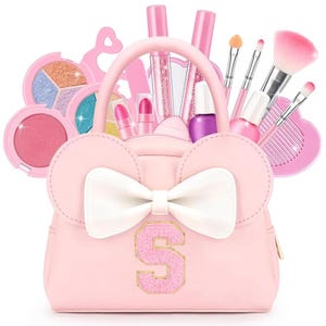 Peut inclure: Un sac à main rose clair avec un nœud blanc et un écusson en forme de lettre S, contenant divers articles de maquillage dont des palettes de fards à paupières, des rouges à lèvres, du vernis à ongles et des pinceaux à maquillage.