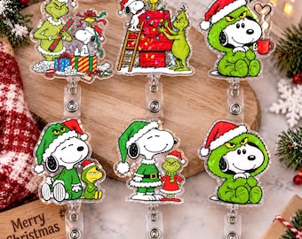 May include: Six acrylic badge reels featuring Snoopy and the Grinch in various Christmas-themed scenes, including decorating a doghouse, wearing green fur costumes, and exchanging gifts, all with a shimmering holographic finish on the surface.