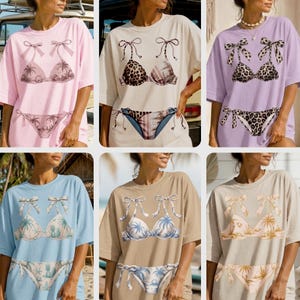 Peut inclure: Une collection de six t-shirts oversize dans diverses couleurs, notamment rose clair, crème, lavande, bleu clair, beige et sable. Chaque t-shirt présente une impression graphique d'un ensemble bikini avec des détails à nouer et des motifs tropicaux.