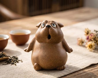 May include: A brown ceramic tea pet figurine shaped like a stout, wide-eyed animal with a surprised expression, featuring a rounded body, small ears, and a small circular opening for a mouth, crafted with a textured, matte clay finish.