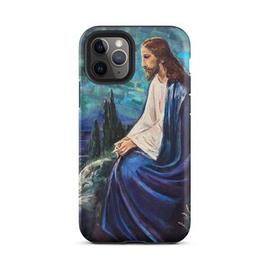 May include: A smartphone case featuring a painted illustration of a figure with long brown hair and a beard, wearing a white tunic and a deep blue cloak. The figure is seated on a rocky landscape with tall cypress trees against a blue sky.