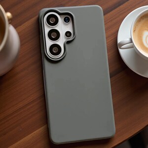 May include: A matte sage green smartphone case featuring a raised, contoured camera cutout that accommodates a multi-lens array. The protective cover has a smooth, solid-colored surface and a precise fit designed for a rectangular mobile device.