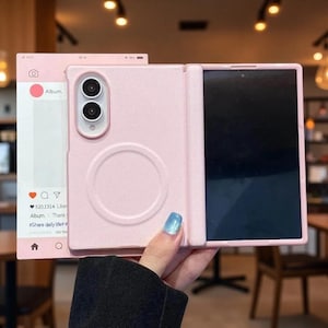 以下が含まれることがあります： デュアルカメラ用の切り抜き、背面の円形磁気充電リング、アイコンとテキストを備えたソーシャルメディアインターフェースを模した装飾パネルが付いた、ライトピンクの折りたたみ式スマートフォンケース。