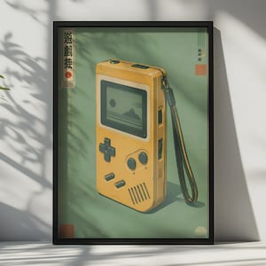 May include: A framed vertical poster featuring a yellow handheld gaming console with a black wrist strap. The screen displays a landscape with a sun and mountains. The background is sage green with Japanese text and geometric red and black accents.