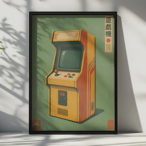 Könnte beinhalten: Ein gerahmtes Poster mit einem gelb-orangen Arcade-Automaten auf einem gedeckten grünen Hintergrund. Der Automat hat einen Joystick, vier Knöpfe und einen Bildschirm. Der japanische Text "遊戲機" steht vertikal in einem weißen Kasten rechts.