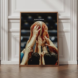 May include: A framed vertical wall art print featuring a basketball held aloft by multiple hands in a stadium setting. The orange basketball is centred, with the text THE PRICE OF GREATNESS printed in white above it against a dark, blurred background.