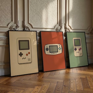 Puede incluir: Tres láminas enmarcadas con ilustraciones de consolas de videojuegos portátiles. La lámina de la izquierda es beige con una consola vertical, la central es naranja con una consola horizontal y la de la derecha es verde salvia con una consola vertical.