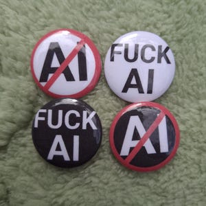 Op de afbeelding: Vier ronde buttons. Twee buttons hebben een witte achtergrond met zwarte tekst FUCK AI. Twee buttons hebben een witte achtergrond met zwarte tekst AI doorgestreept door een rode diagonale lijn en een rode cirkelvormige rand.