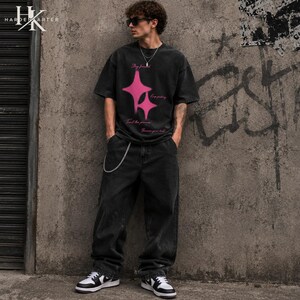 May include: A charcoal gray short-sleeve t-shirt featuring two bright pink four-pointed star graphics and pink cursive text that reads Stay focused, Keep pushing, Trust the process, Become your best, paired with loose-fit charcoal gray denim jeans.