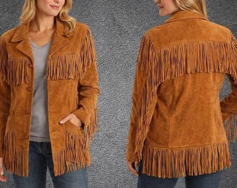 May include: A tan suede jacket featuring long fringe detailing across the chest, back, and sleeves. The jacket has a collared neckline, a button-front closure, and two front pockets. The design includes a straight hemline with fringe trim.