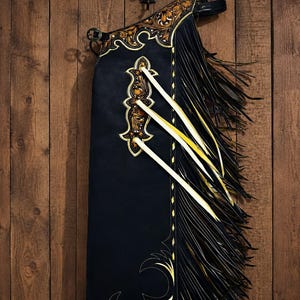 Svarta läderchaps, western cowboychaps med svarta fransar, guldfärgade blommönster i läder med rodeochaps