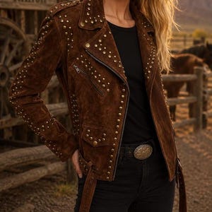 May include: A dark brown suede motorcycle jacket featuring an asymmetrical front zipper, a notched lapel, and multiple rows of metallic studs along the sleeves, shoulders, and front panels. The jacket includes a buckled belt at the waist.