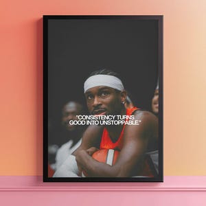 May include: A framed wall art print featuring a basketball player wearing a white headband and an orange jersey, holding a basketball. The text "CONSISTENCY TURNS GOOD INTO UNSTOPPABLE" is printed in white capital letters over the dark background.