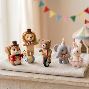 Könnte beinhalten: Ein Set aus fünf nadelgefilzten Tierfiguren, bestehend aus einem Eichhörnchen in roter Jacke, einem Löwen auf einem Ball, einem Bären auf einem Einrad, einem Elefanten mit Partyhut und einem Hasen mit Hula-Hoop-Reifen, arrangiert als Zirkus-Szene.