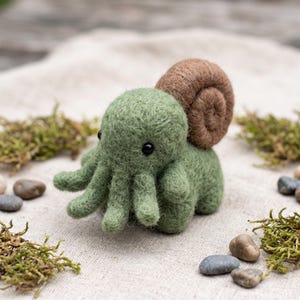 May include: A needle-felted creature featuring a light green body with multiple tentacles, small black bead eyes, and a large, coiled brown shell on its back. The texture of the wool is visible throughout the entire surface of the figure.