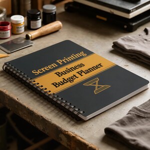 Può includere: Un quaderno a spirale con copertina nera e una fascia orizzontale dorata. Il testo recita Screen Printing Business Budget Planner in caratteri neri. Un'icona a forma di clessidra in linee dorate è posizionata sotto il testo.
