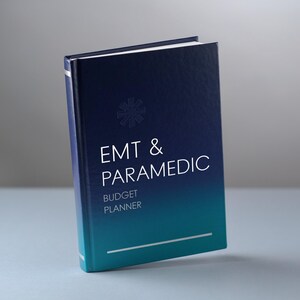 May include: A hardbound budget planner with a dark blue to teal gradient cover. The front features a star of life emblem, the text "EMT & PARAMEDIC BUDGET PLANNER" in white, and a thin horizontal white line near the bottom edge of the book.