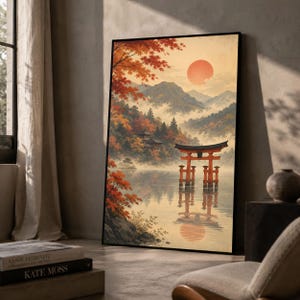 Può includere: Una stampa artistica da parete incorniciata che raffigura un paesaggio sereno con un portale torii rosso che sorge in acque calme. La scena presenta montagne nebbiose, vibranti aceri autunnali arancioni e rossi e un grande sole pallido in un cielo soffuso.