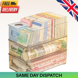 May include: A stack of three clear plastic storage bins with integrated handles. The top bin holds various rectangular paper pads. The middle bin contains multiple rolls of patterned adhesive tape. The bottom bin stores a collection of flat notebooks.