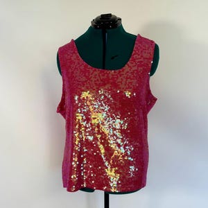 May include: A sleeveless, sequined top in a vibrant fuchsia color. The sequins have an iridescent quality, with hints of gold and green. The top is displayed on a green dress form against a white background.