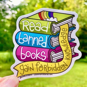 May include: A sticker featuring a stack of three books in green, blue, and pink, with the words "Read banned books gain forbidden knowledge." A yellow banner with the word "knowledge" is draped over the books. A rainbow is on the top book.