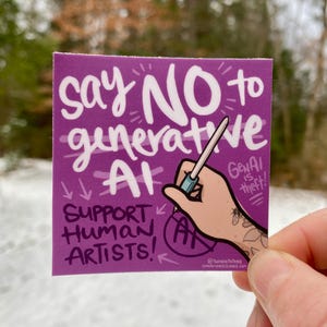 May include: A purple square sticker with white text that reads "Say NO to generative AI." The sticker also says "Support Human Artists!" and "AI is theft!" A hand with a tattoo is holding a pen.