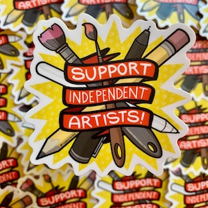 Puede incluir: Una pegatina con un dise&ntilde;o de estrella amarilla que presenta materiales de arte como pinceles, l&aacute;pices y bol&iacute;grafos. Una pancarta roja en el centro dice "SUPPORT INDEPENDENT ARTISTS!" en texto blanco. La pegatina es un llamado a apoyar a los artistas.