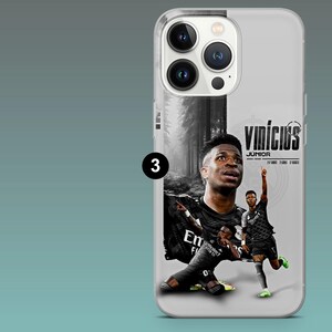 May include: A clear smartphone case featuring a graphic of soccer player Vin&iacute;cius J&uacute;nior. The design includes a black and white forest background, the text Vin&iacute;cius J&uacute;nior, and two images of the player in a black jersey celebrating a goal.