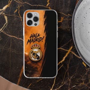 May include: A clear phone case featuring a split design with a textured orange background on the left and a solid black section on the right. The text HALA MADRID! is printed in black above the official Real Madrid crest with a gold crown.