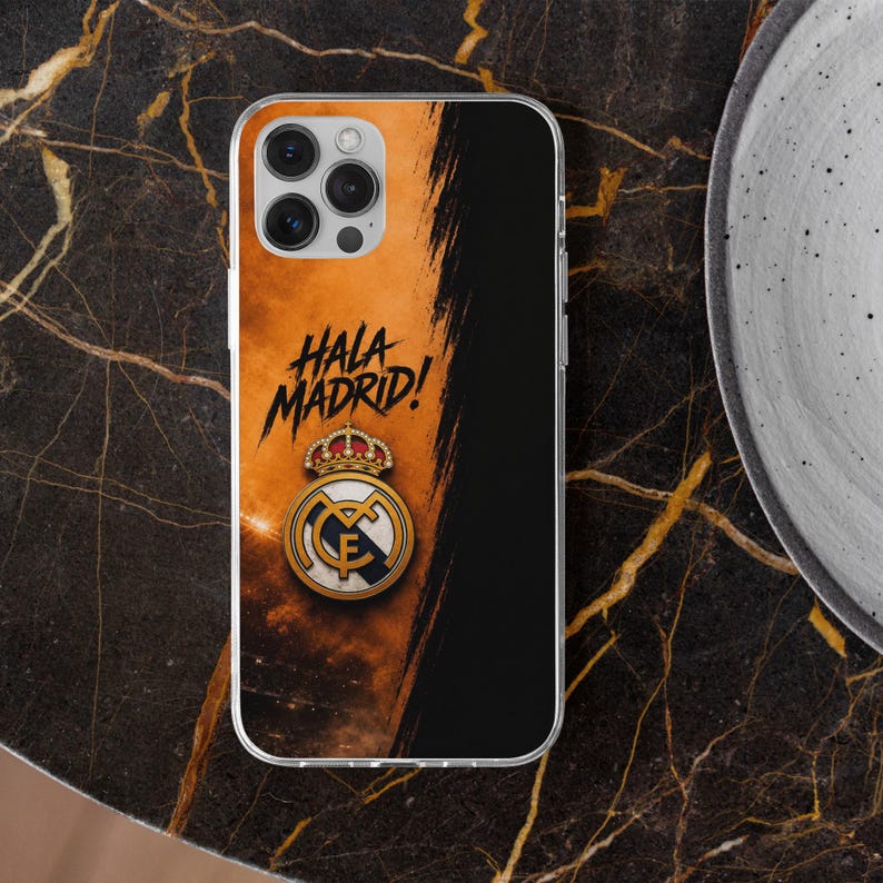 May include: A clear phone case featuring a split design with a textured orange background on the left and a solid black section on the right. The text HALA MADRID! is printed in black above the official Real Madrid crest with a gold crown.