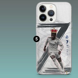 May include: A white smartphone case featuring a graphic of a soccer player wearing a white jersey with the text Emirates Fly Better, a red crown, and the number 7. The design includes a large black brushstroke number 7 and the text VINI JR.
