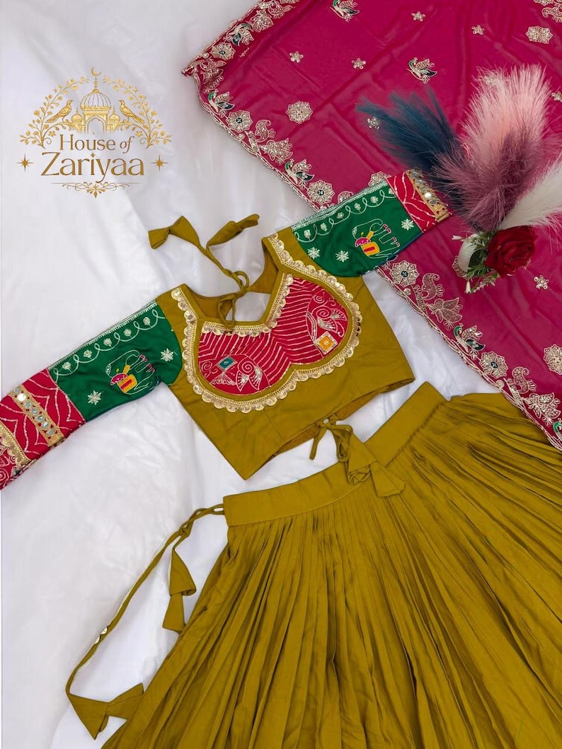 May include: A mustard yellow pleated skirt paired with a matching long-sleeved blouse featuring green sleeves, red patterned panels, and gold trim. A separate magenta fabric piece with intricate silver embroidery and a floral border is included.