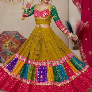 May include: A mustard yellow lehenga choli set featuring a long, pleated skirt with a multi-colored patchwork hem in purple, blue, green, and yellow, finished with a wide magenta border. The long-sleeved blouse has pink and green patterned accents.
