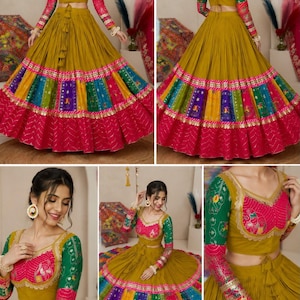 May include: A mustard yellow lehenga choli set featuring a cropped blouse with green and pink patterned sleeves, and a long, pleated skirt with a wide, multi-colored panel border in blue, yellow, and green, finished with a solid pink hem.