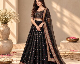 May include: A black lehenga choli set featuring a cropped blouse with intricate embroidery and a floor-length skirt adorned with small floral motifs. The ensemble includes a sheer black dupatta with a wide, ornate border in gold, red, and silver.