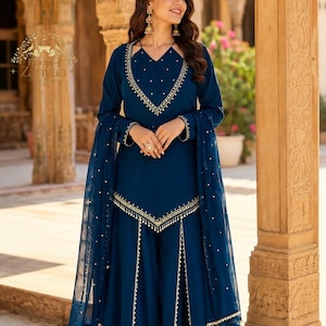 May include: A deep blue long-sleeved tunic and wide-leg pants set featuring gold embroidery and small white bead accents along the neckline, hem, and pant panels. A matching sheer blue dupatta with scattered white beads completes the ensemble.