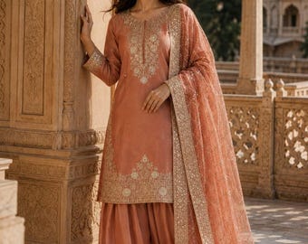 May include: A peach-coloured salwar kameez set featuring a long-sleeved tunic with intricate gold embroidery around the neckline and hem, paired with matching loose-fitting trousers and a sheer, gold-embellished dupatta with a decorative border.