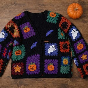 May include: A long-sleeved cardigan made of black yarn featuring a patchwork of colorful crochet granny squares. The squares display various Halloween-themed motifs including orange pumpkins, white ghosts, purple bats, and yellow stars.
